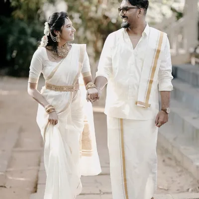 An elegant walking shot of a couple in traditional Kerala attire, a white mundu and saree, capturing a moment of grace and cultural pride.
