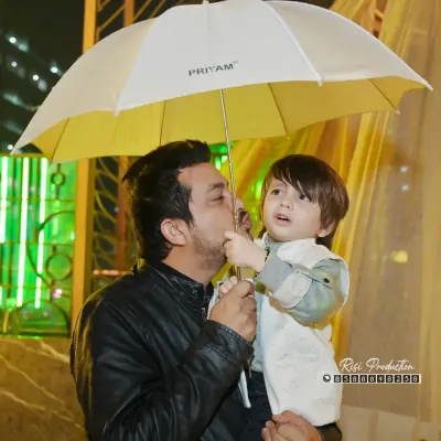 A tender moment between a father and son, sheltered under an umbrella. This artistic shot beautifully captures the protective and loving bond they share.