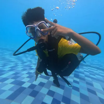 A young participant gives a cool sign underwater during his first scuba experience in a pool. Our introductory courses are all about building confidence safely.