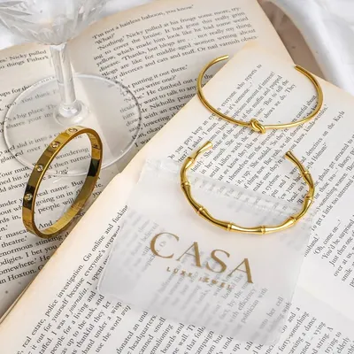 An aesthetic flatlay of gold bracelets styled on an open book with a wine glass. This type of editorial product photography is perfect for creating a sophisticated and literary brand image.
