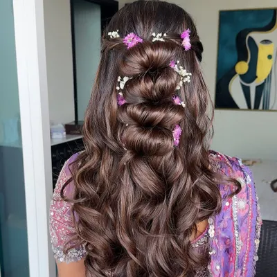 A beautiful half-updo with a twisted bun and soft waves, adorned with lilac and white flowers to match the bride's outfit.