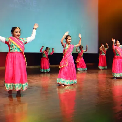 A vibrant group of our young dancers in colorful pink costumes during their semi-classical performance at Pehal. Their coordinated movements and happy expressions capture the spirit of the event.