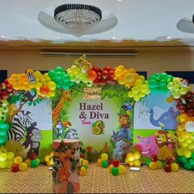 A vibrant and classic jungle theme stage setup for Hazel & Diva's 5th birthday. This backdrop is filled with friendly jungle animals and surrounded by a colorful balloon arch.