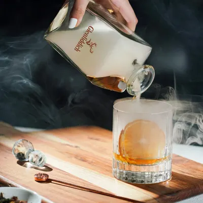 A dramatic pour of smoky whisky into a glass with a perfect ice sphere. This shot uses theatrical smoke and precise lighting to create a luxurious and high-end feel for the brand.