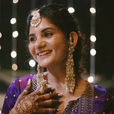 A happy client smiling through her Mehendi ceremony. We customized these iconic pearl tassel earrings and a matching bindiya to complement her vibrant purple outfit, creating a look that's both classic and full of personality.