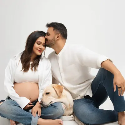 An expecting couple shares a quiet moment with their beloved dog resting its head on the mother's lap. This studio maternity portrait shows that family includes our furry members too.