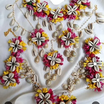 A complete Haldi jewellery set made with artificial flowers and cowrie shells. This set includes a necklace, earrings, maang tikka, and hathphool for a complete look.