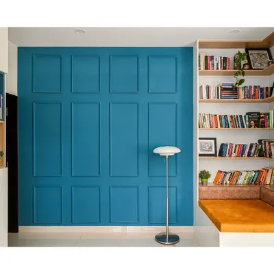 I designed this cozy reading corner to be a perfect escape. It features custom-built corner shelves for an extensive book collection and a comfortable cushioned seat, set against a bold blue paneled accent wall.