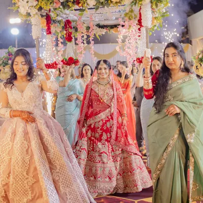 A grand bridal entry under a beautiful floral 'phoolon ki chaadar'. The bride looks regal in her heavily embroidered red lehenga, a classic choice for a North Indian wedding ceremony.
