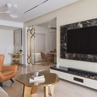 The living room in our "Guilded Grace" project, featuring a statement black marble TV wall, fluted paneling, and warm tan leather armchairs for a touch of classic comfort.
