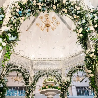 Looking up into a floral arch, where lush greenery and blooms are expertly woven into a white lattice structure, with a chandelier sparkling at the center.