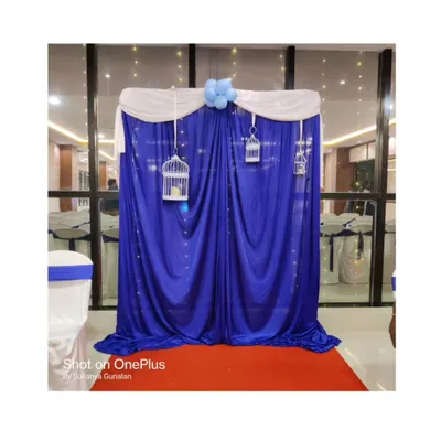 A simple and elegant photo booth setup. The royal blue curtain backdrop is accented with white draping, fairy lights, and decorative birdcages, creating a perfect spot for pictures.