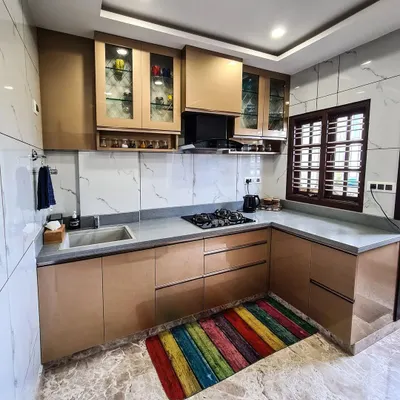 An L-shaped modular kitchen with a sophisticated color palette. The cabinets have a metallic bronze finish, paired with a grey countertop and a white marble-patterned backsplash, creating a modern and luxurious cooking space.