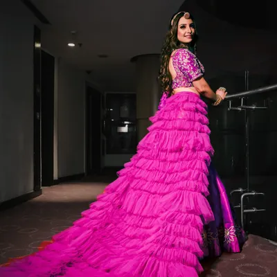 This shot of an anchor in a magnificent ruffled lehenga showcases the drama of the outfit. The long train creates a stunning visual, and the pose highlights both the dress and her confident look.