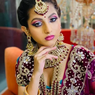 A regal North Indian bridal look featuring a dramatic smokey eye with a pop of pink and purple. The makeup is paired with heavy kundan and pearl jewellery for a truly royal feel.
