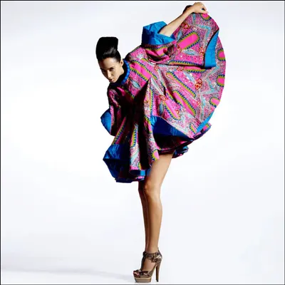 A high-fashion editorial shot for Harper's Bazaar. The model's dynamic pose and the flowing, colorful fabric create a sense of movement and sculptural beauty against a clean white background.