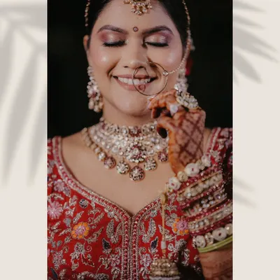 A stunning close-up of the bride, highlighting her intricate jewelry, flawless makeup, and the rich embroidery of her red lehenga. This is a perfect example of a fine art bridal portrait.