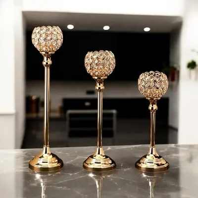 A set of three crystal and gold candle holders of varying heights. The faceted crystal balls catch and reflect light beautifully, making them a glamorous gift or decor item for a reception desk or event.