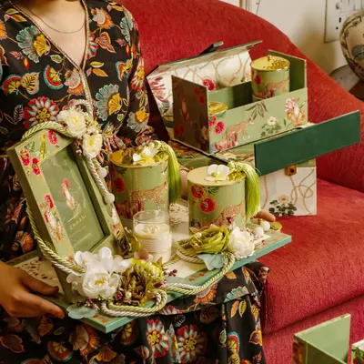 A client holding a tray filled with goodies from the Tales of Tropic collection. This shows how the hamper can be presented, with a photo frame, candles, and artisanal jars all featuring the lush, botanical design.