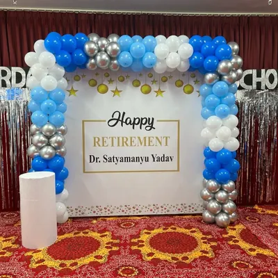 A beautiful setup for a retirement party. This decoration features a custom 'Happy Retirement' backdrop framed by a blue, white, and silver balloon arch.
