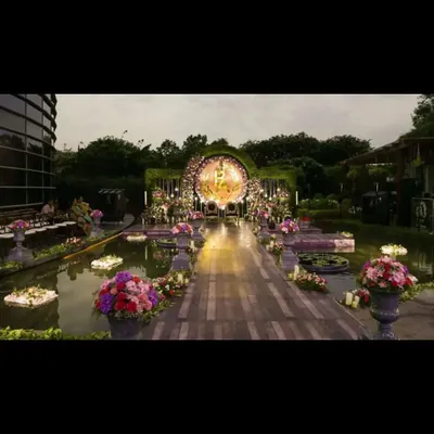 A truly magical wedding ceremony setup over a serene water body. This destination wedding design features a floating walkway, lush floral arrangements, and a stunning circular mandap, creating an unforgettable experience as dusk settles.
