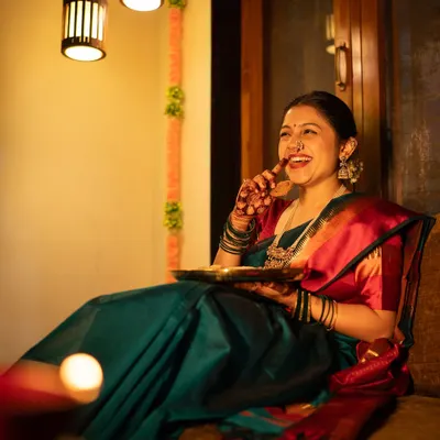 A candid shot of pure laughter during a Diwali photoshoot. Dressed in a beautiful teal and red saree, she enjoys a piece of 'faral', perfectly capturing the happy and relaxed atmosphere of the festival of lights.