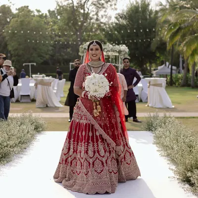 She wore hope, grace, and a promise that forever is hers. A classic bridal entry shot, capturing the bride in her magnificent red lehenga as she walks down the aisle at her Thailand wedding.