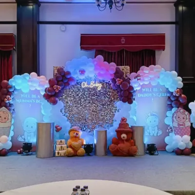 A modern 'Oh Baby' themed decoration for a gender reveal party. The setup includes a silver sequin wall, a neon sign, and balloon arrangements in pink and blue on either side.