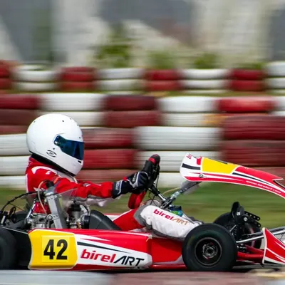 A driver in our Birel ART kart executes a turn with precision, showcasing the vehicle's agility and grip. The motion blur in the background emphasizes the high speed of competitive karting.