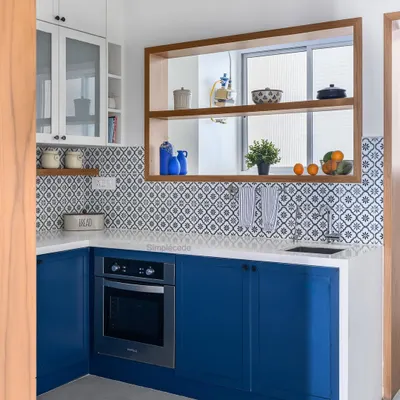 This Parisian-inspired kitchen features royal blue base cabinets and white overhead units, complemented by patterned backsplash tiles. A custom wooden frame around the utility window adds a warm, classical touch.