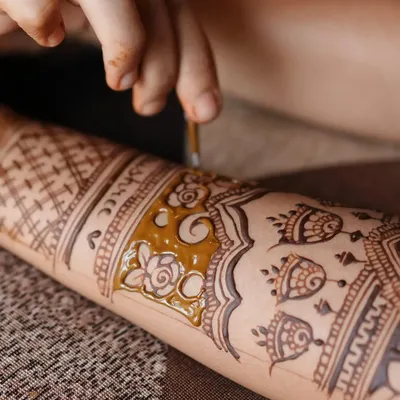 A macro shot of the mehendi application. You can see the fine tip of the cone creating delicate floral and bell (jhumki) details on the arm.