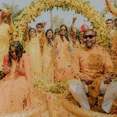 A shower of flower petals marks the climax of a fun-filled Haldi. This wide shot captures the collective joy of family and friends celebrating the couple under a beautiful floral arch.