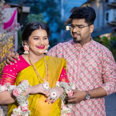 A candid, loving moment between the expecting couple during their outdoor baby shower celebration. The partner gently holds the mother-to-be, who is glowing in a yellow saree and floral jewelry, sharing a happy, private glance.