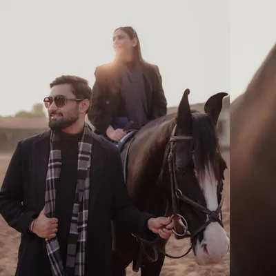A stylish equestrian-themed shoot. The groom leads the horse while the bride sits elegantly, both dressed in chic black winter wear, creating a sophisticated and unique pre-wedding portrait.