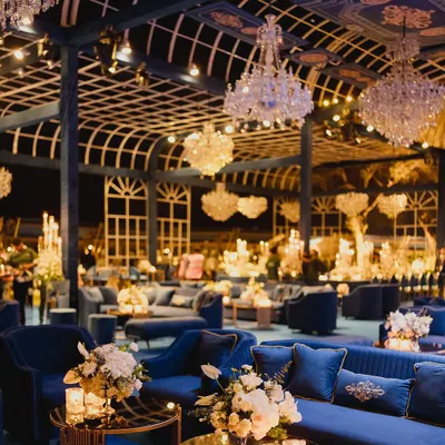 A wide view of the magnificent gala, showcasing the seamless integration of luxurious blue velvet seating, ambient candlelight, and grand floral arrangements. Every element is designed to create a cohesive and opulent environment for a high-end corporate event.