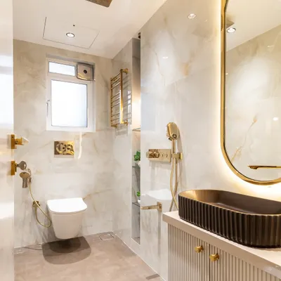 Luxury in every little detail. This contemporary bathroom blends serene white and beige-toned tiles with opulent gold fittings, creating a space that feels both refreshing and indulgent. The sleek SS mirror frame adds a crisp modern edge.