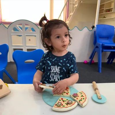 Our little stars learn best when they are involved. Here, a child is engaged in a pretend play activity with a wooden pizza set, which helps in developing social and fine motor skills.