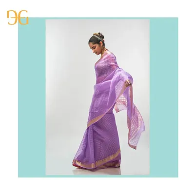 The delicate, airy quality of this African Violet silk organza saree is evident in its graceful movement. The gold zari checks catch the light, adding a subtle shimmer to the beautiful drape.