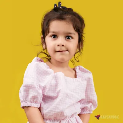 A charming close-up portrait of a young girl against a vibrant yellow background. The soft lighting and her direct, sweet expression make this a perfect shot for a kid's portfolio or family album.
