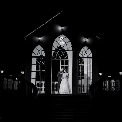 A dramatic and timeless black and white shot of the couple at the entrance of a grand building. The strong silhouettes and architectural lines create a powerful, cinematic image.