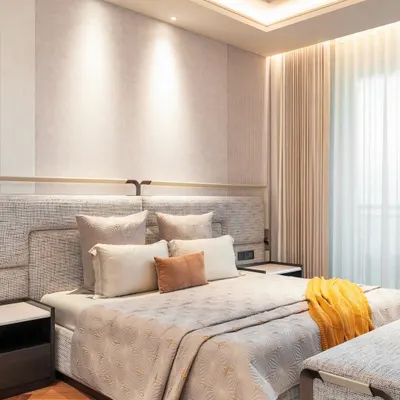 A serene and luxurious master bedroom featuring a custom-designed upholstered headboard that extends across the wall. Integrated side tables and warm, layered lighting create a cohesive and restful environment. The soft textures and neutral palette are accented by a pop of yellow for warmth.
