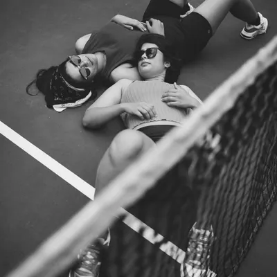 An unconventional portrait of two people on a tennis court. The high angle and the lines of the court create a strong graphic composition, focusing on a moment of shared stillness.