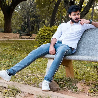 A relaxed outdoor portrait of a man sitting on a park bench. The natural setting and his casual pose create a candid and approachable feel for this men's portfolio shot.