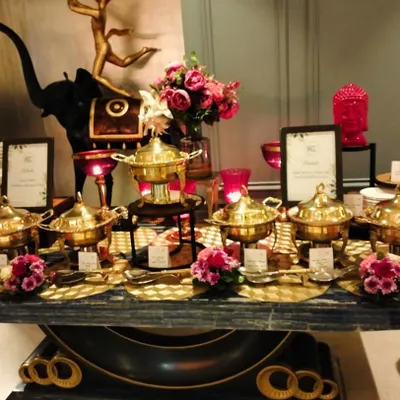 An opulent Indian food buffet featuring our signature brass serving dishes. The setup is enhanced with elegant floral arrangements and decorative pieces, creating a truly luxurious feel for a house party.