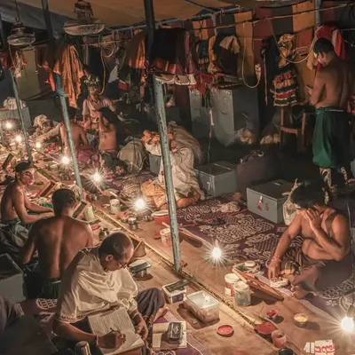 A wide view of the entire backstage area, or 'chowki'. You can see multiple artists at different stages of preparation, costumes hanging, and the focused, communal atmosphere that exists before the show begins.