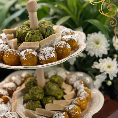 A tiered stand of traditional Indian sweets, or mithai, featuring pistachio barfi and motichoor ladoo, elegantly dusted with silver varq.