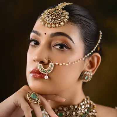 A close-up of a North Indian bridal look, focusing on the intricate nath (nose ring) and maang tikka. The eye makeup is sharp and defined, with a glossy lip to balance the look.