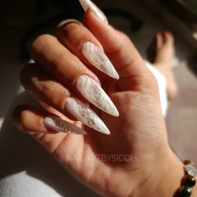 A set of dramatic, extra-long stiletto nails with an encapsulated white marble and foil design, showing the beautiful shape and length that can be achieved.