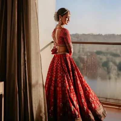 A bride in her magnificent red lehenga, taking a quiet moment on the balcony to look out at the view. This silhouette against the morning light creates a breathtaking and pensive portrait.
