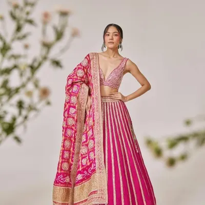 A vision in pink. This stunning lehenga features a striped skirt and a heavily embroidered blouse, paired with a traditional bandhani dupatta for a look that is both modern and classic.